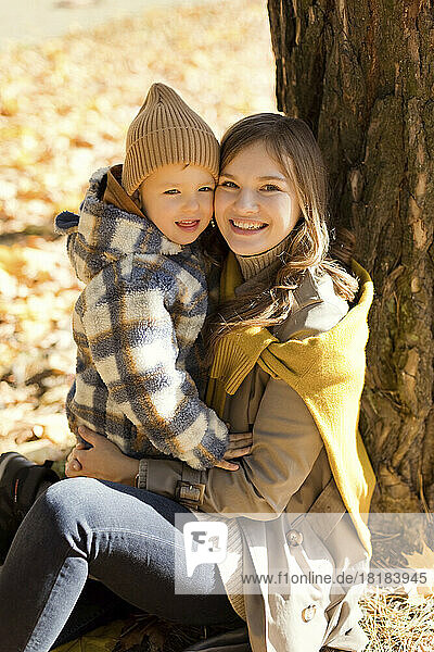Happy mother and cute boy sitting near tree in park