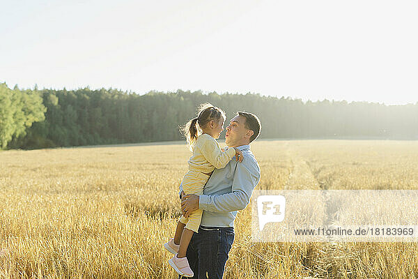 Father carrying daughter in field on sunny day