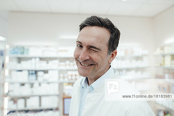 Happy pharmacist in lab coat winking at store