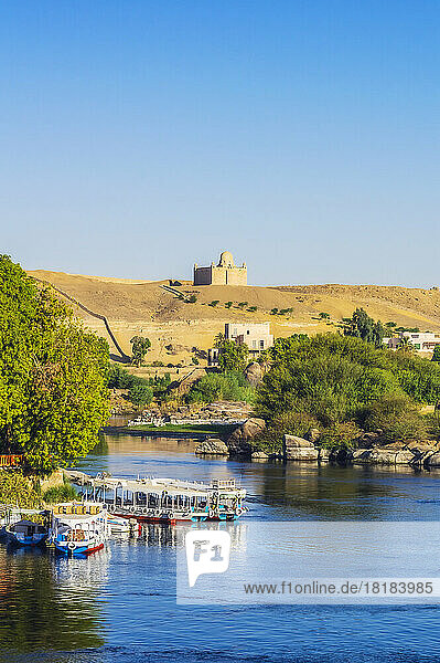 Egypt  Aswan Governorate  Aswan  Tourboats moored on bank of Nile river with Mausoleum of Aga Khan in background