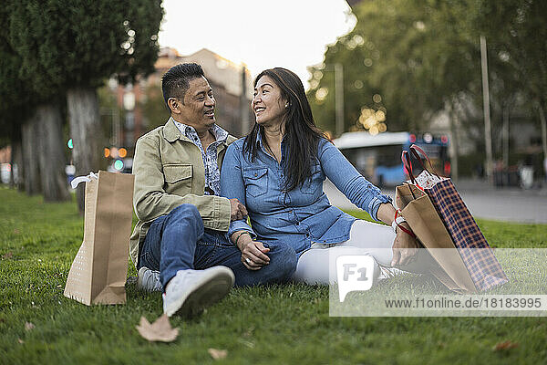Lächelndes älteres Paar mit Einkaufstüten sitzt auf Gras im Park
