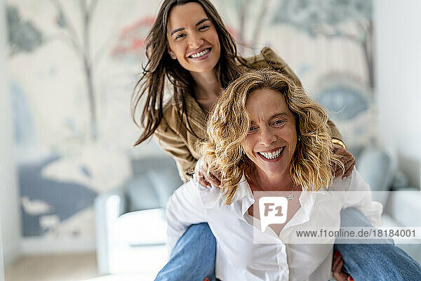 Cheerful mother enjoying and giving piggyback ride to daughter at home