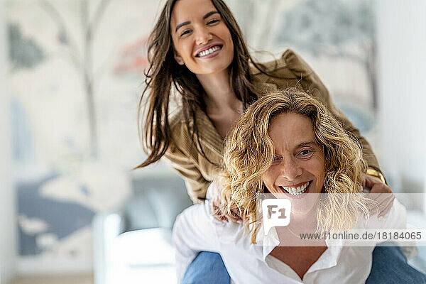 Happy mature woman enjoying and giving piggyback ride to daughter at home
