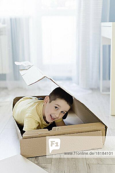 Smiling boy hiding in box at home