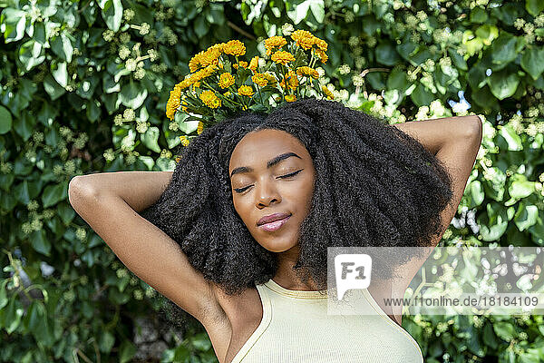 Woman with eyes closed holding yellow flowers in front of plant
