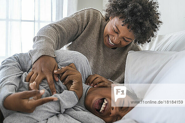 Happy mother tickling boy on bed at home