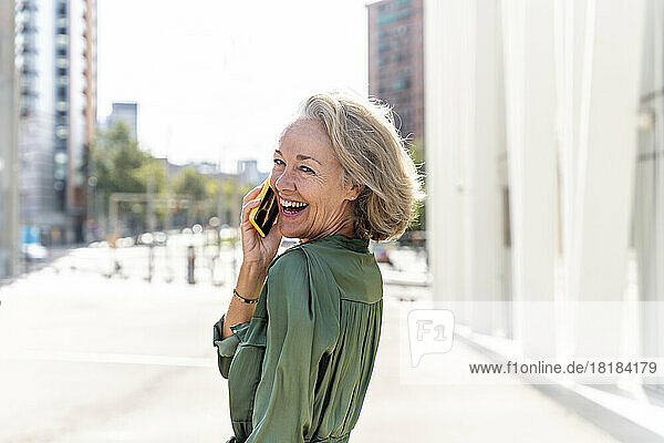 Happy mature woman talking through smart phone on sunny day