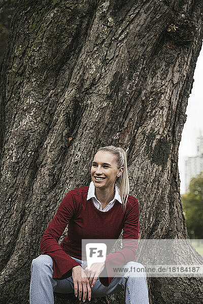 Happy young woman sitting in front of tree