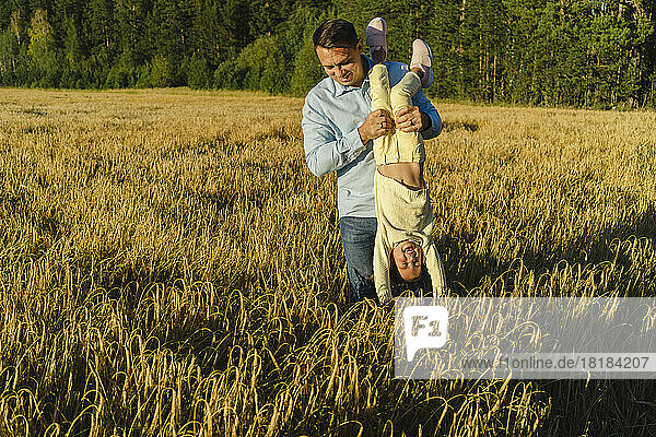 Father holding daughter upside down in field on sunny day