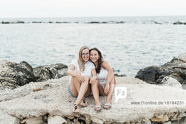 Happy friends sitting together on rock at beach