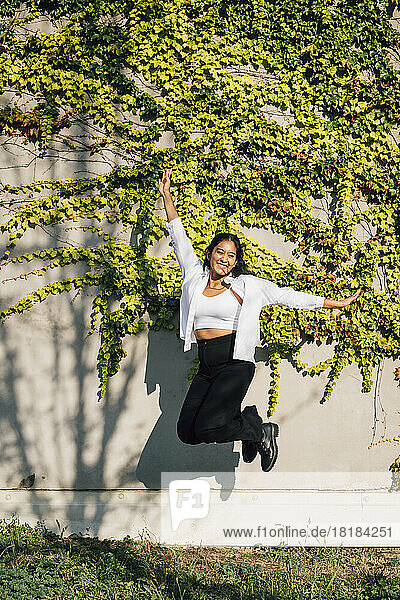 Happy young woman jumping in front of wall