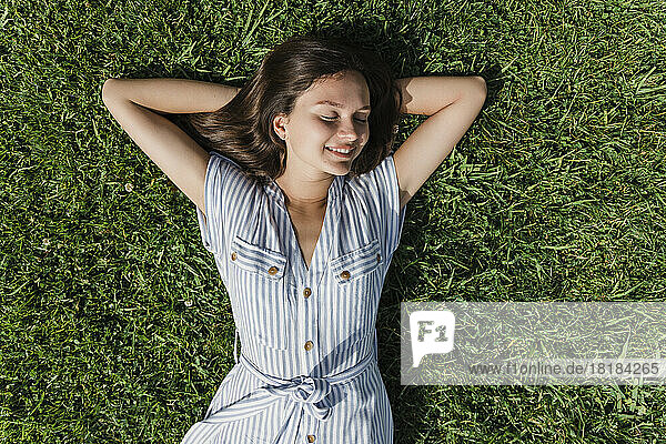 Glückliche junge Frau mit geschlossenen Augen entspannt sich im Gras