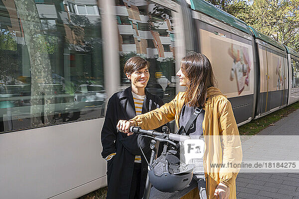 Smiling young woman looking at friend standing by passing tram