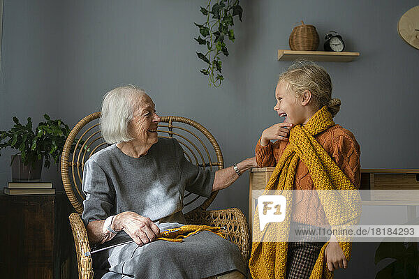 Glückliche Seniorin blickt zu Hause auf Enkelin mit Strickschal