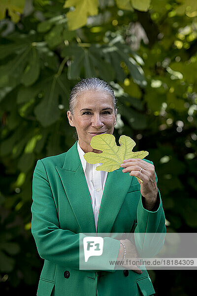 Smiling senior woman wearing green coat holding fig leaf