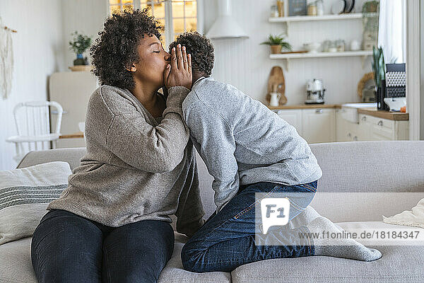 Mother whispering into son's ear at home