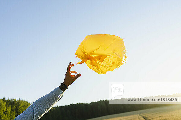 Die Hand eines Mannes greift auf dem Feld nach einem Müllsackballon