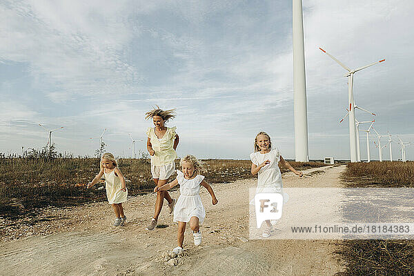 Glückliche Frau läuft mit Töchtern vor Windkraftanlagen