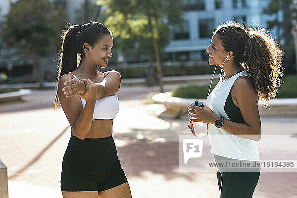 Smiling teenage girl exercising and talking to friend on sunny day