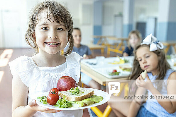 Smiling student holding healthy meal on plate standing at cafeteria