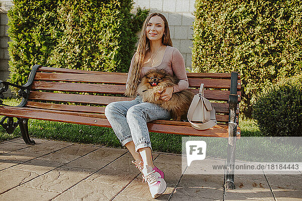 Smiling woman with dog sitting on bench in park