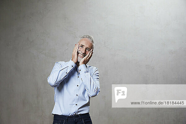 Happy man touching face standing in front of grey background