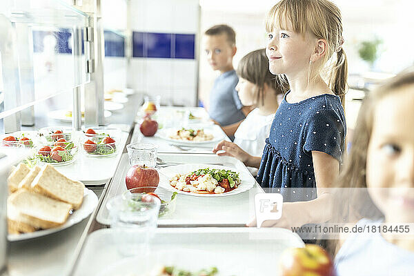 Girl with blond hair holding lunch tray at school cafeteria