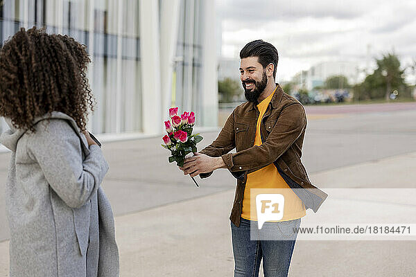 Happy young man giving bouquet of flowers to woman at footpath