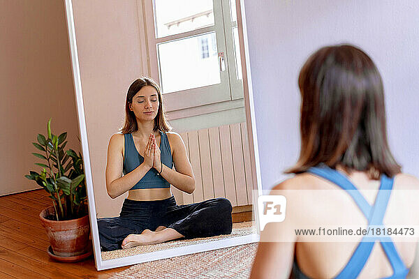 Young woman doing yoga reflecting on mirror at home