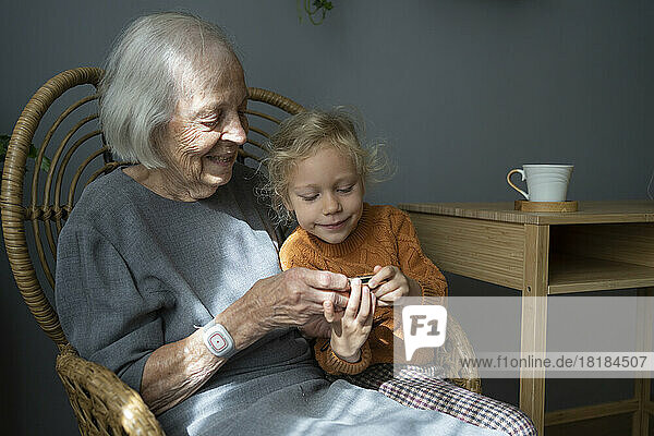 Glückliche Großmutter mit Enkelin  die auf einem Stuhl in die Kamera blickt