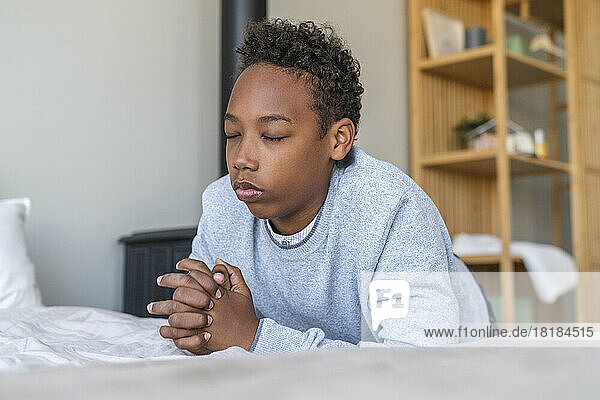 Boy with eyes closed praying by bed at home