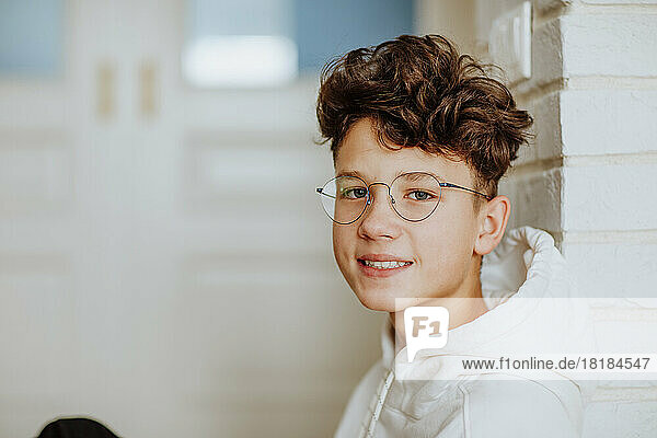 Smiling boy wearing eyeglasses leaning on wall