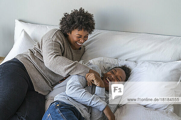 Mother tickling son lying on bed at home