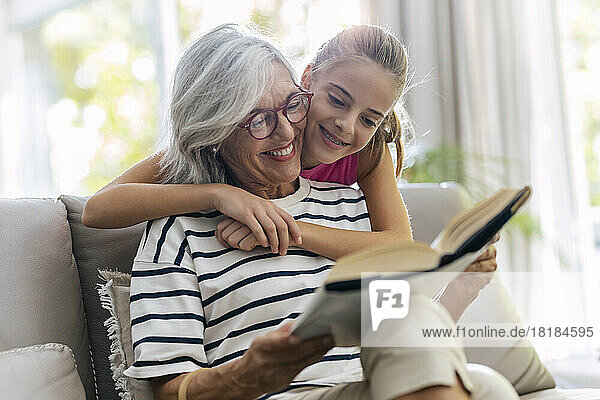 Grandmother reading book with granddaughter on sofa at home