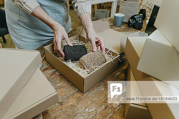 Hands of mature craftswoman packing crochet decor in box on workbench