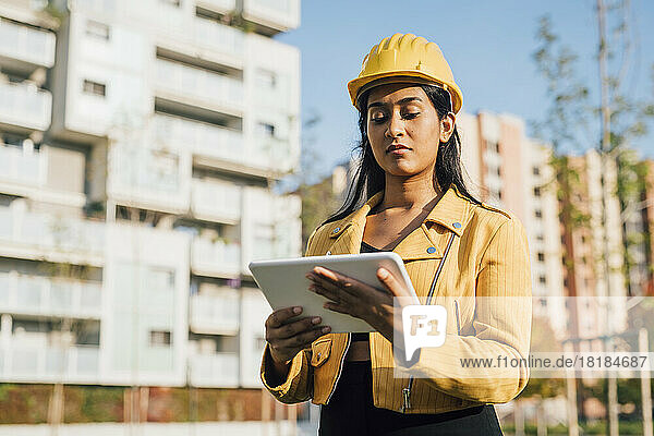 Woman wearing hardhat using tablet PC in front of buildings