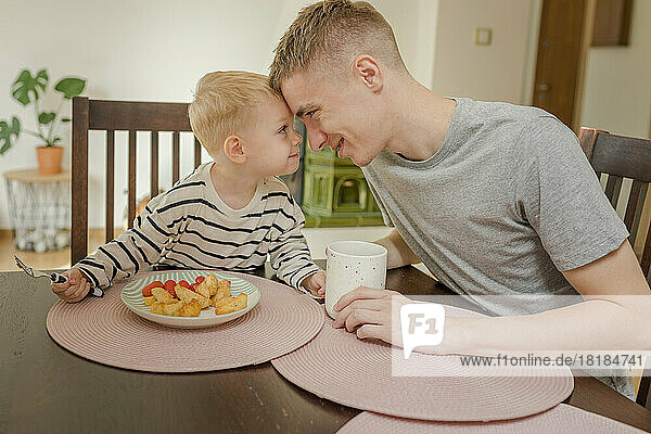 Happy father and son touching foreheads at dining table