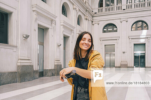 Lächelnde Frau mit Tretroller am städtischen Gebäude