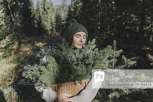 Woman with eyes closed holding basket of spruce twigs at forest