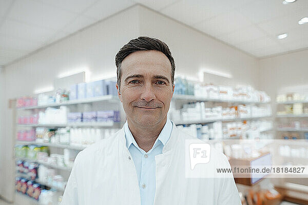 Smiling pharmacist in front of medicines shelf at pharmacy