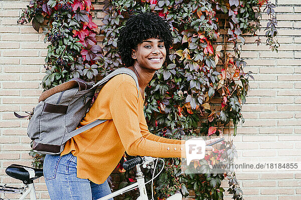 Smiling woman with backpack holding mobile phone on cycle