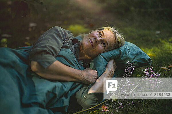 Thoughtful mature woman lying on grass in garden