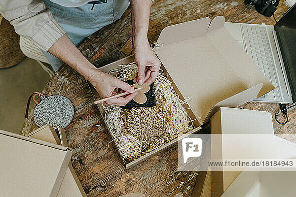 Hands of craftswoman writing on postcard above crochet decor in box