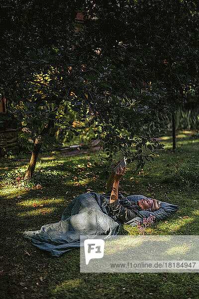 Woman lying on grass reading book in garden