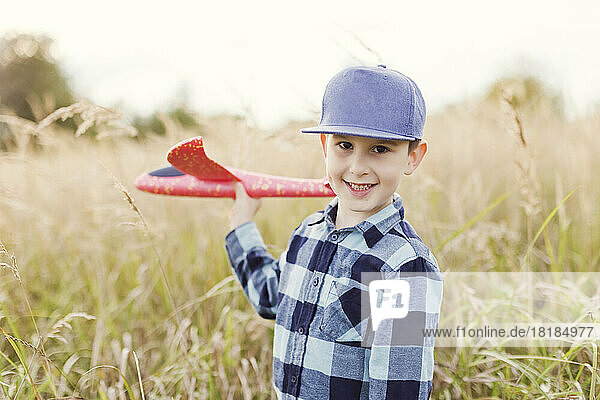 Smiling boy with cap holding toy airplane in field