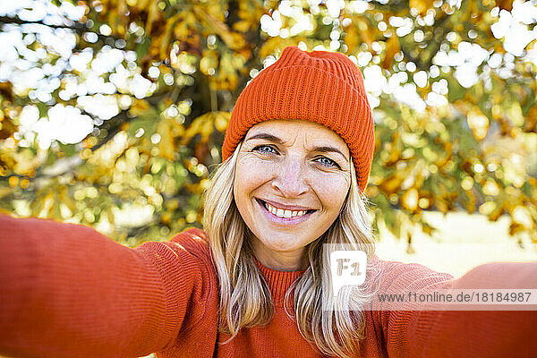 Lächelnde reife Frau mit orangefarbener Strickmütze macht am Wochenende ein Selfie