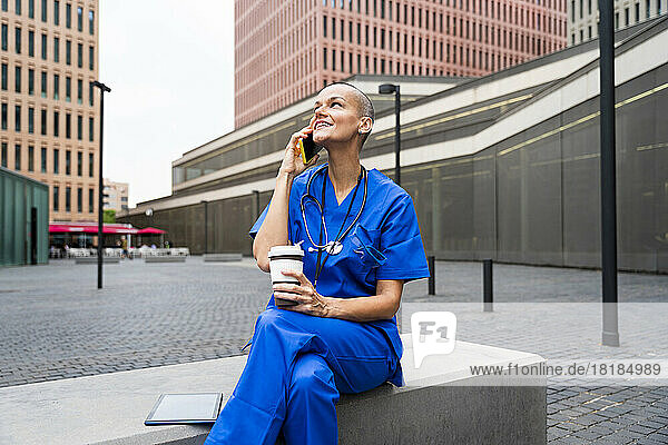 Smiling mature female nurse taking through smart phone sitting on bench