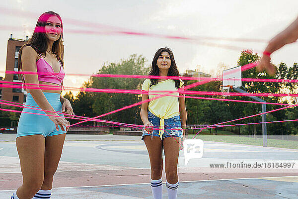 Smiling woman with friend holding pink string at sports court