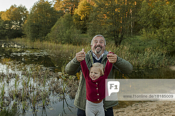 Smiling man lifting granddaughter near lake