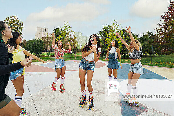 Happy young woman with friends wearing roller skate dancing at sports court